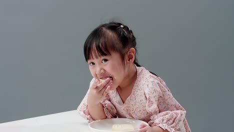 Niño-Asiático-Comiendo-Dulce-En-El-Estudio-Con-Un-Fondo-Gris