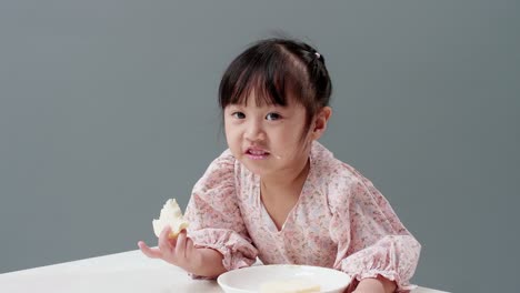 Niño-Asiático-Comiendo-Dulce-En-El-Estudio-Con-Un-Fondo-Gris