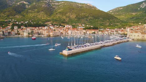 Panorama-of-a-coastal-town-with-many-houses-with-red-roofs,-surrounded-by-the-sea-and-mountains-with-long-pier