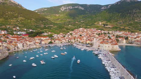 Panorama-of-a-coastal-town-with-many-houses-with-red-roofs,-surrounded-by-the-sea-and-mountains-with-yachts-in-marina-bay-and-Bell-tower-and-pier