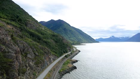 Aerial-view-of-car-driving-road-along-Alaskan-coast,-Turnagain-arm