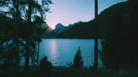 Silueta-De-Fotógrafo-Sentado-Tranquilamente-En-El-Bosque-Mirando-Una-Hermosa-Puesta-De-Sol-Detrás-De-Las-Montañas-En-El-Lago-Achensee-En-Austria-Europa-En-Vista-Amplia