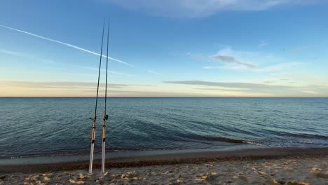 Two-Fishing-Rods-Standing-On-The-Sand-With-Seascape-In-Background