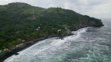 Aerial-view-full-shot,-scenic-view-of-waves-rushing-to-the-shores-of-the-bitcoin-beach-in-El-Salvador,-Mexico,-mountain-and-blue-sky-in-the-background