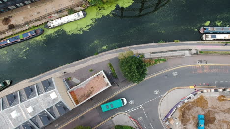 Ariel-view-of-regents-canal-in-east-London-with-canal-boats,-vehicle-on-quiet-road-and-cyclists-riding-by