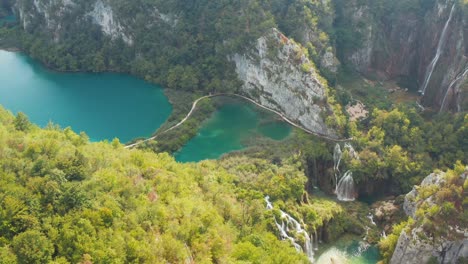 Incredible-aerial-drone-view-of-bright-turquoise-lakes-connected-with-waterfalls-between-rocky-cliffs-and-dense-forest