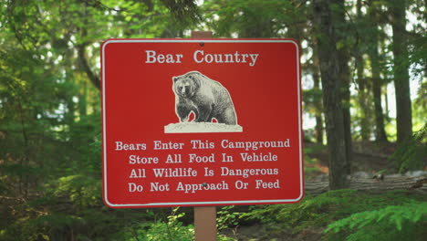 A-Bear-Country-warning-sign-near-a-road-inside-Glacier-National-Park,-Montana,-U