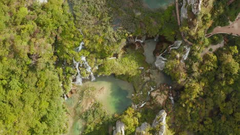 Incredible-aerial-drone-top-down-view-of-bright-turquoise-lakes-connected-with-waterfalls-between-rocky-cliffs-and-dense-forest