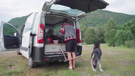 Kaukasischer-Mann-Und-Sein-Haustier-Alaskan-Malamute-Camping-Mit-Gepackten-Sachen-Auf-Der-Rückseite-Des-Minivans