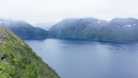 Hombre-De-Pie-En-Una-Montaña-Rocosa-Con-Una-Magnífica-Vista-General-Del-Lago-Tranquilo-Cerca-De-Segla-En-Senja,-Noruega