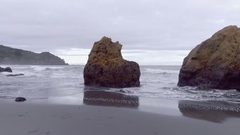 Elevándose-Desde-Un-Cúmulo-De-Rocas-Para-Revelar-Una-Playa-Aislada-En-La-Salvaje-Y-Escarpada-Costa-Este-De-Nueva-Zelanda