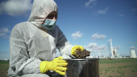 Scientist-in-protective-suit-checking-oil-contamination-in-ground,-industrial-background,-outdoor-wide-angle-view