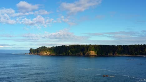 Stunning-aerial-drone-shot-of-the-gorgeous-Third-Beach-in-Forks,-Washington-with-a-forest-or-large-green-pine-trees-on-cliffs-on-a-warm-sunny-summer-morning-with-clouds