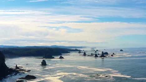 Stunning-dolly-out-aerial-drone-shot-of-the-gorgeous-Third-Beach-in-Forks,-Washington-with-large-rock-formations,-cliffs,-small-waves-and-sea-foam-on-a-warm-sunny-summer-morning