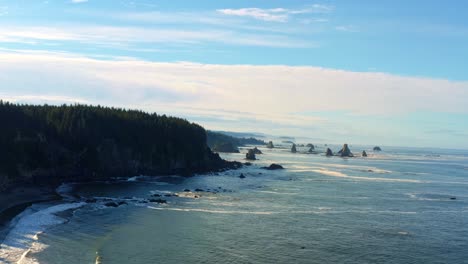 Stunning-aerial-drone-trucking-right-shot-of-the-gorgeous-Third-Beach-in-Forks,-Washington-with-large-rock-formations,-cliffs,-small-waves-and-sea-foam-on-a-warm-sunny-summer-morning