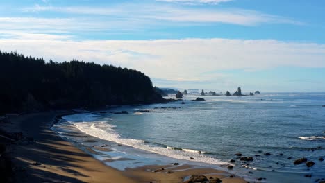 Stunning-aerial-drone-rising-shot-of-the-gorgeous-Third-Beach-in-Forks,-Washington-with-large-rock-formations,-surrounded-by-a-pine-tree-forest-on-cliffs,-and-golden-sand-on-a-warm-summer-morning
