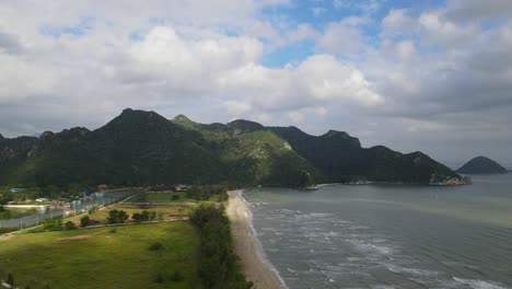 Aerial-footage-sliding-towards-the-left-revealing-sunlight-falling-on-the-beach-front-and-the-estuarine-river-with-the-fishing-village,-Sam-Roi-Yot-National-Park,-Prachuap-Khiri-Khan,-Thailand