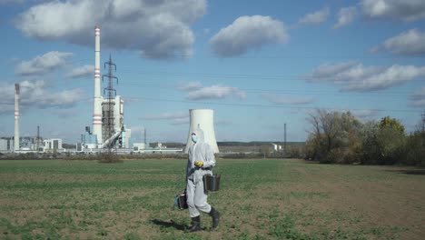 Scientist-in-protective-suit-and-suitcase-walking-field-outdoors,-power-station-or-industrial-background,-ecological-disaster-concept