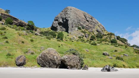 Panning-shot-of-vast-mountain-with-green-meadow-and-empty-sandy-beach-during-beautiful-sunny-day-with-blue-sky-at-Spirits-Bay,New-Zealand