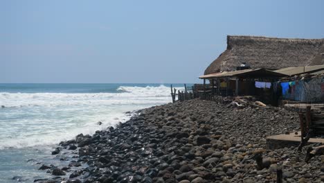 Ganzaufnahme,-Malerischer-Blick-Auf-Die-Hütte-Am-Felsigen-Strand-Am-Bitcoin-Strand-In-El-Salvador,-Mexiko,-Hohe-Wellen-Und-Strahlend-Blauer-Himmel-Im-Hintergrund