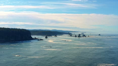Stunning-aerial-drone-trucking-right-shot-of-the-gorgeous-Third-Beach-in-Forks,-Washington-with-large-rock-formations,-cliffs,-small-waves-and-sea-foam-on-a-warm-sunny-summer-morning