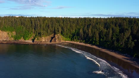 Stunning-aerial-drone-dolly-in-shot-of-the-gorgeous-Third-Beach-in-Forks,-Washington-with-a-forest-or-large-green-pine-trees-on-cliffs-on-a-warm-sunny-summer-morning-with-clouds