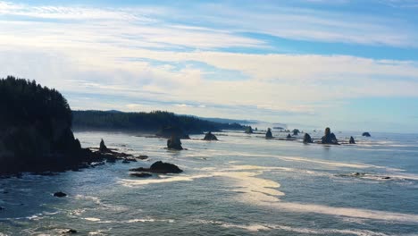 Stunning-trucking-right-aerial-drone-shot-of-the-gorgeous-Third-Beach-in-Forks,-Washington-with-large-rock-formations,-cliffs,-small-waves-and-sea-foam-on-a-warm-sunny-summer-morning