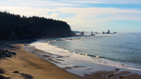 Stunning-descending-aerial-drone-shot-of-the-gorgeous-Third-Beach-in-Forks,-Washington-with-large-rock-formations,-cliffs,-small-waves-and-golden-sand-on-a-warm-sunny-summer-morning