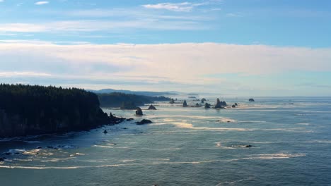 Stunning-aerial-drone-dolly-in-shot-of-the-gorgeous-Third-Beach-in-Forks,-Washington-with-large-rock-formations,-cliffs,-small-waves-and-sea-foam-on-a-warm-sunny-summer-morning
