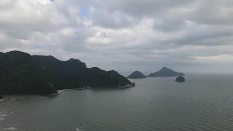 Reverse-aerial-footage-revealing-mountains-and-islands-and-waves-rushing-to-the-shore-during-a-cloudy-day-in-Sam-Roi-Yot-National-Park,-Prachuap-Khiri-Khan,-Thailand