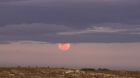 Rise-of-a-full-glowing-red-moon-with-clouds-above-the-horizon-of-the-earth