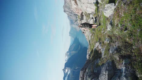 Vertikale-Aufnahme-Von-Wanderern-Und-Hunden,-Die-Auf-Einem-Felsigen-Berg-Klettern-Und-Im-Sommer-Einen-Majestätischen-Blick-Auf-Den-See-Bieten