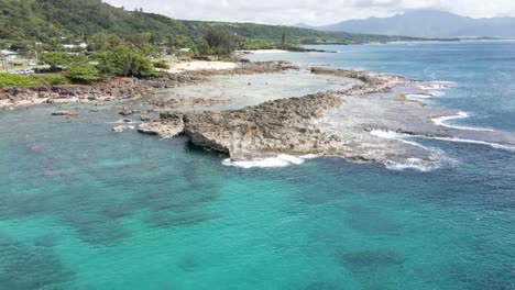 Aerial-footage-off-the-coast-of-the-tropical-Island-of-Hawaii-featuring-Shark's-Cove-with-lots-of-rocky-shoreline-and-clear-blue-emerald-green-ocean-water-on-the-coast-with-tropical-forests