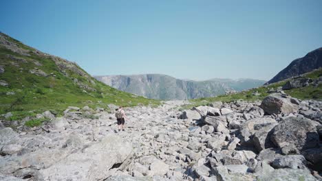 Backpacker-Walking-On-A-Terrain-With-Large-Rocks-Overlooking-Mardalsfossen-Waterfall-In-Norway
