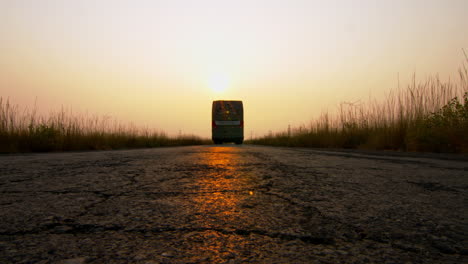 Ein-Bus,-Der-Bei-Sonnenuntergang-Mitten-Auf-Einer-Landstraße-über-Eine-Kamera-Fährt