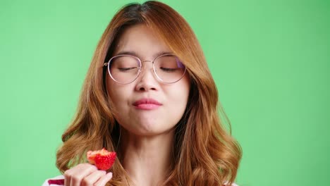 Young-woman-enjoying-strawberry-in-the-studio-with-green-screen-chroma-key-background