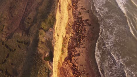 Slow-motion-shot-of-the-Cliffs-at-sunset,-beautiful-top-down-view-of-the-water-waves-moving-too-and-fro-in-Acantilados-Mar-del-Plata,-South-America