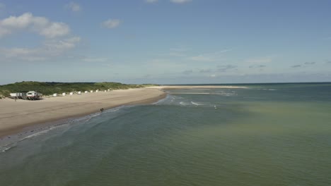 Aerial-shot-of-waves-hitting-a-white-beach-at-Oranjezon-nature-reserve-in-Zeeland,-the-Netherlands,-on-a-beautiful-sunny-day
