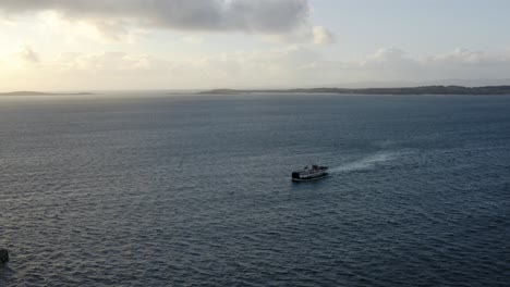AERIAL---Ferry-ship-arriving-at-sunrise-to-Isle-of-Gigha,-Kintyre,-Scotland,-forward
