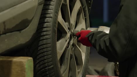 Close-up-of-mechanic's-hands-with-red-gloves-screwing-a-wheel-with-automatic-screwdriver