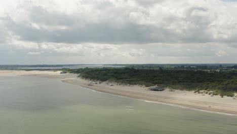 Aerial-shot-approaching-a-beach-pavilion-on-an-empty-white-beach-in-the-beautiful-Oranjezon-nature-reserve-in-Zeeland,-the-Netherlands