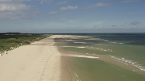 Aerial-shot-flying-backwards-over-waves-hitting-a-beautiful-quiet,-white-beach-on-a-sunny-day