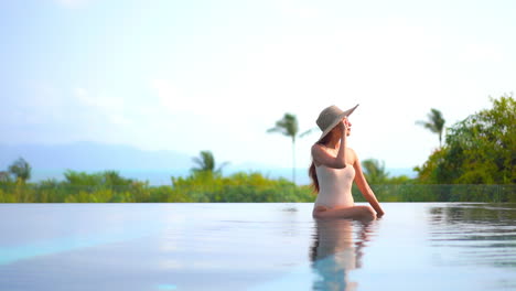 Während-Sie-Am-Rand-Eines-Resort-infinity-pools-Sitzt,-Passt-Eine-Attraktive-Frau-Ihre-Sonnenbrille-An