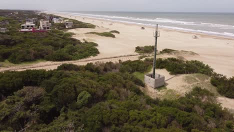 Circling-close-up-shot-of-the-green-antenna-in-front-to-the-ocean-which-is-close-to-the-town-beach-at-Mar-de-las-Pampas,-Argentina