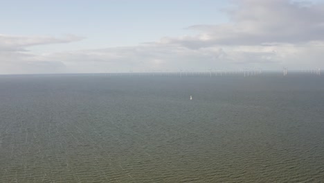 Aerial-shot-of-a-sailboat-nearing-a-large-wind-farm-at-sea-in-the-Netherlands-on-a-beautiful-sunny-day