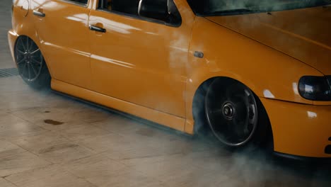 Yellow-shiny-tuned-car-in-a-garage-drifts-into-place-and-creates-white-smoke-from-the-tires