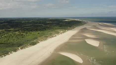 Aerial-shot-flying-over-green-dunes,-a-white-beach,-sand-dunes-and-the-sea-on-a-beautiful-sunny-day