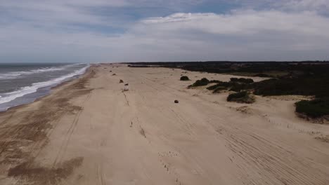 Vehicles-driving-along-sandy-beach,-Mar-de-las-Pampas-in-Argentina
