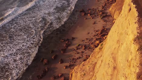 Top-down-aerial-view-of-beach-over-cliff-edge-during-sunset