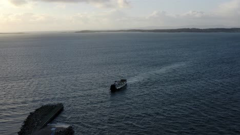 AERIAL---Ferry-ship-leaving-the-Isle-of-Gigha,-Kintyre,-Scotland,-pan-left